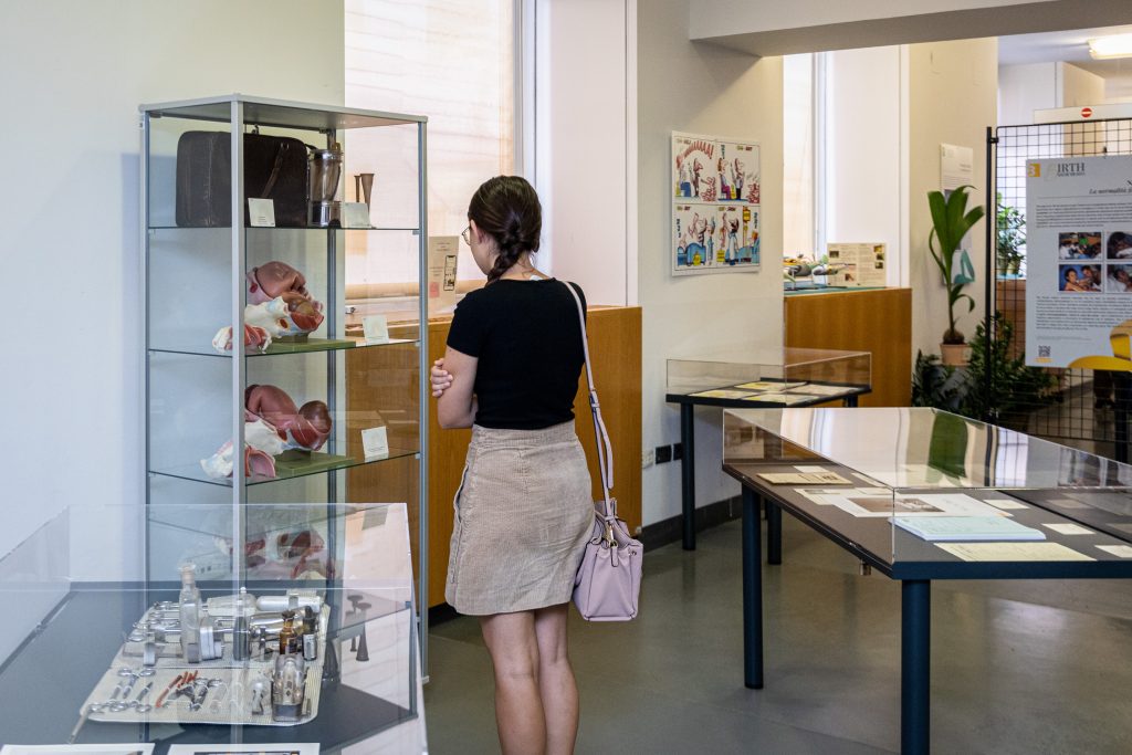Una visitatrice di spalle che osserva il contenuto di una teca dove ci sono dei modelli ostetrici che mostrano il momento del parto
