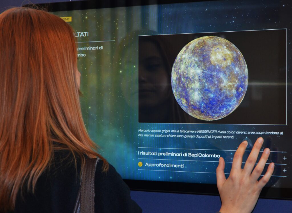 Ragazza dai capelli rossi vista di profilo mentre fruisce i contenuti della mostra "Osservatori del cielo".